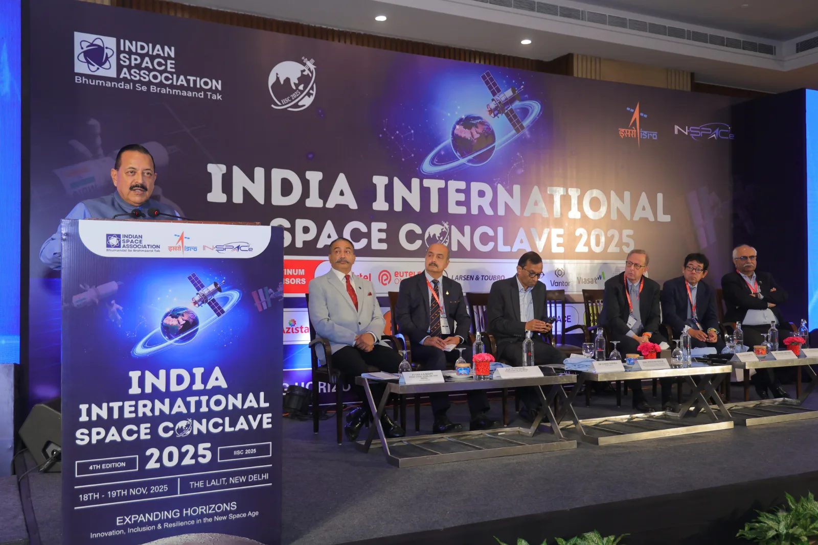 A speaker addresses IISC 2025 from the podium as panellists listen on stage beneath the India International Space Conclave 2025 backdrop.